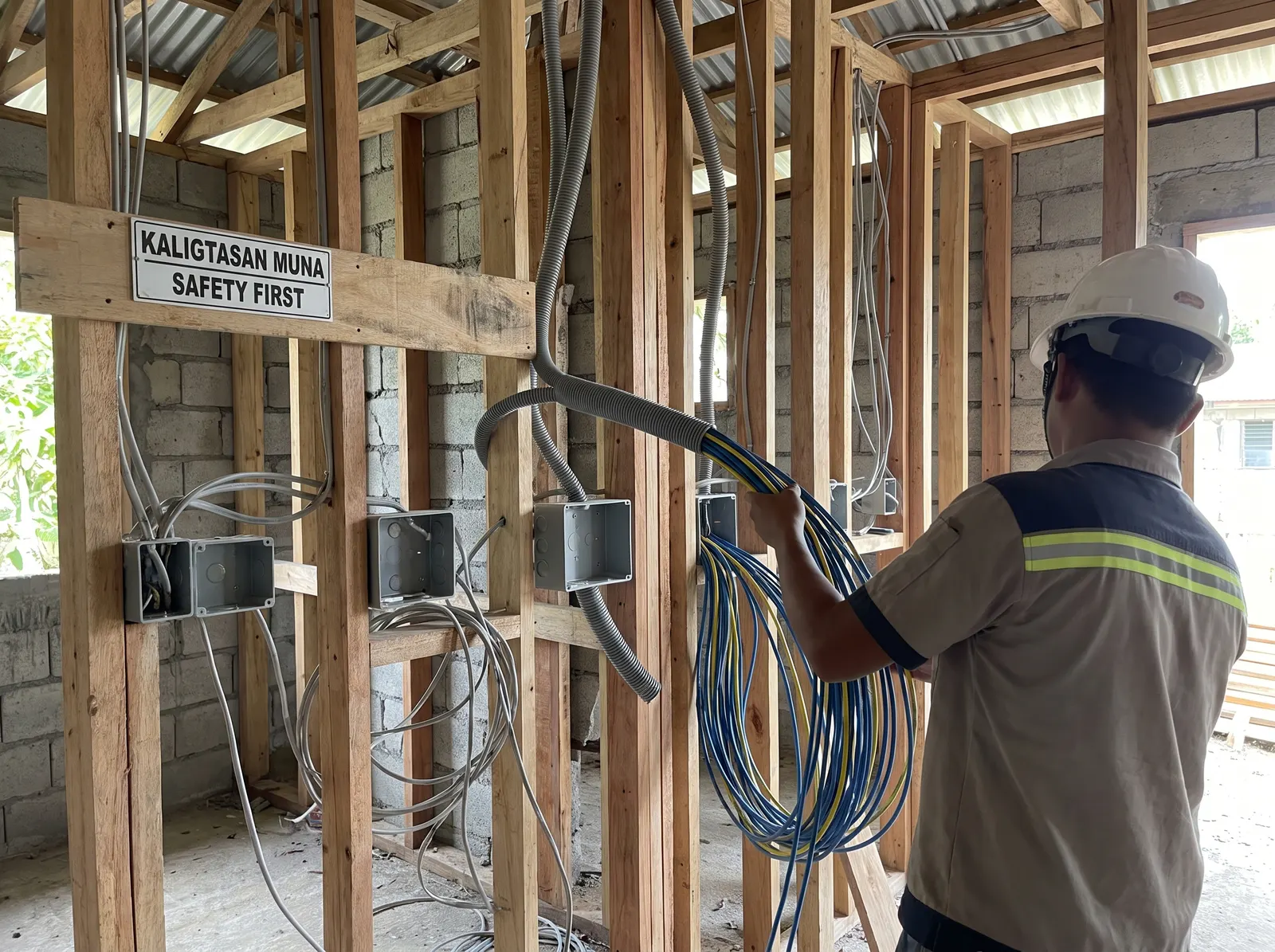 Electrician pulling cable through open conduit and wall studs before drywall closes up, with junction boxes and raw wiring runs visible.